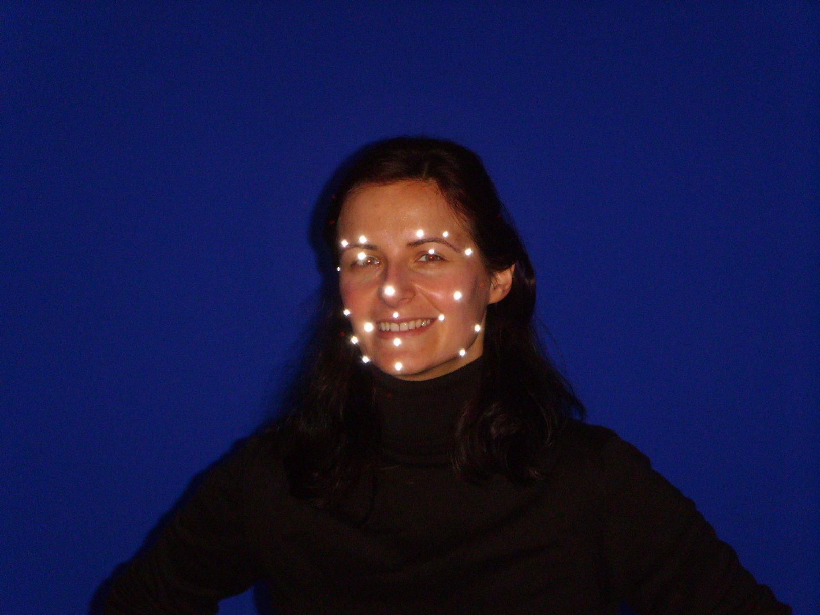 Close-up of a performer's facial marker array against the blue cyclorama